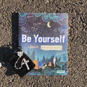 Photo of Be Yourself Journal on road with a rosary laying on top of it