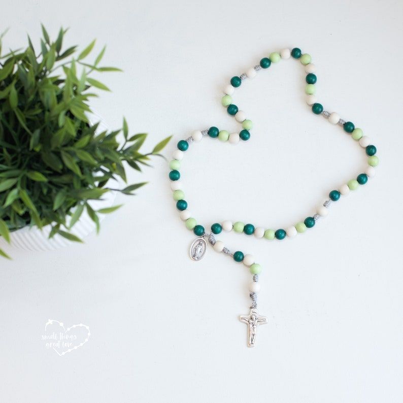Green and white rosary next to a plant