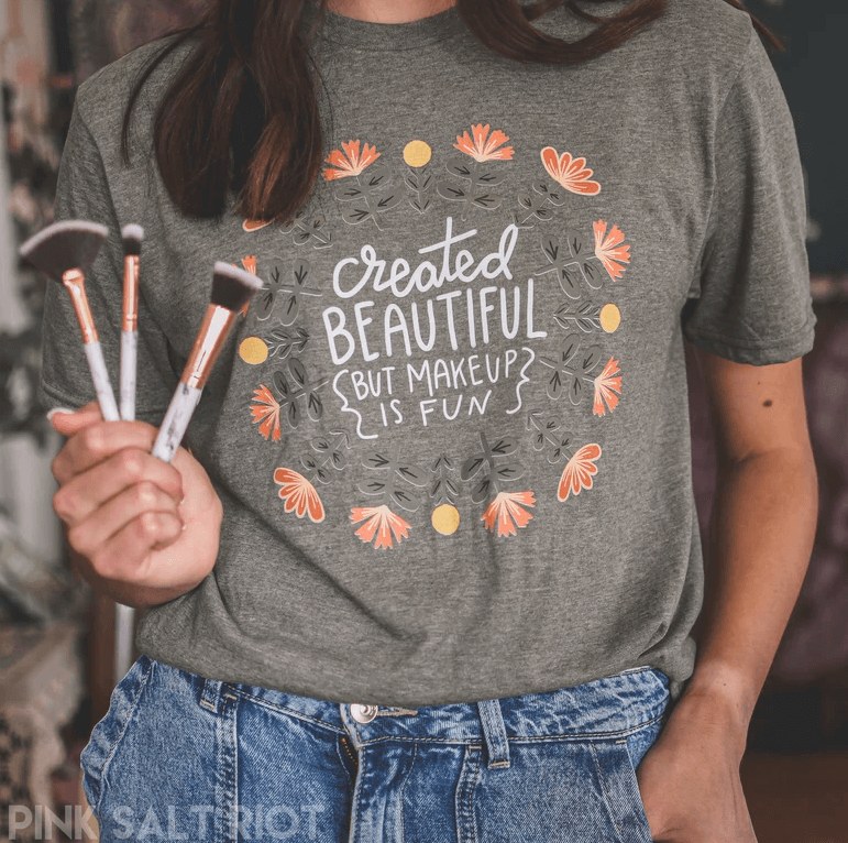 Showing you the shirt that says created beautiful but makeup is fun