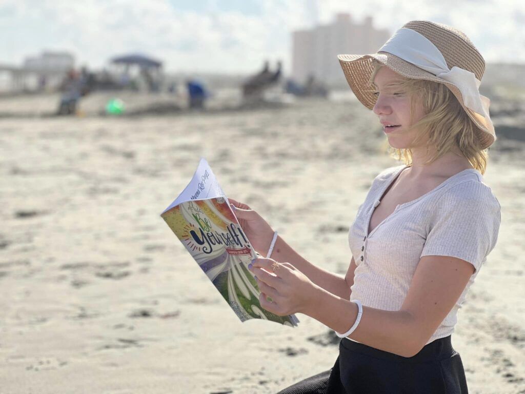 Young girl reading Be Yourself book on beach