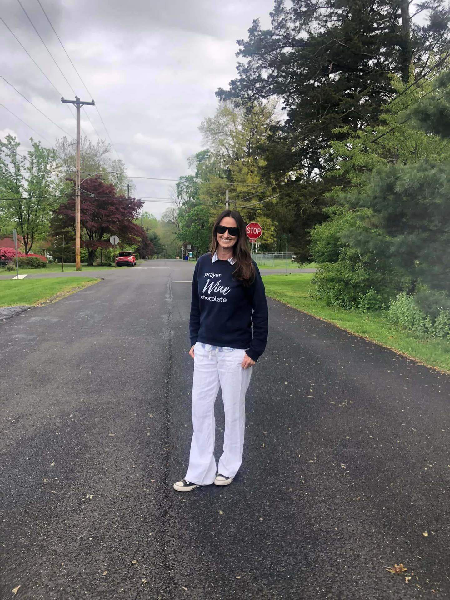 Amy Brooks standing in the middle of a road wearing a navy Prayer Wine Chocolate sweatshirt with white pants.