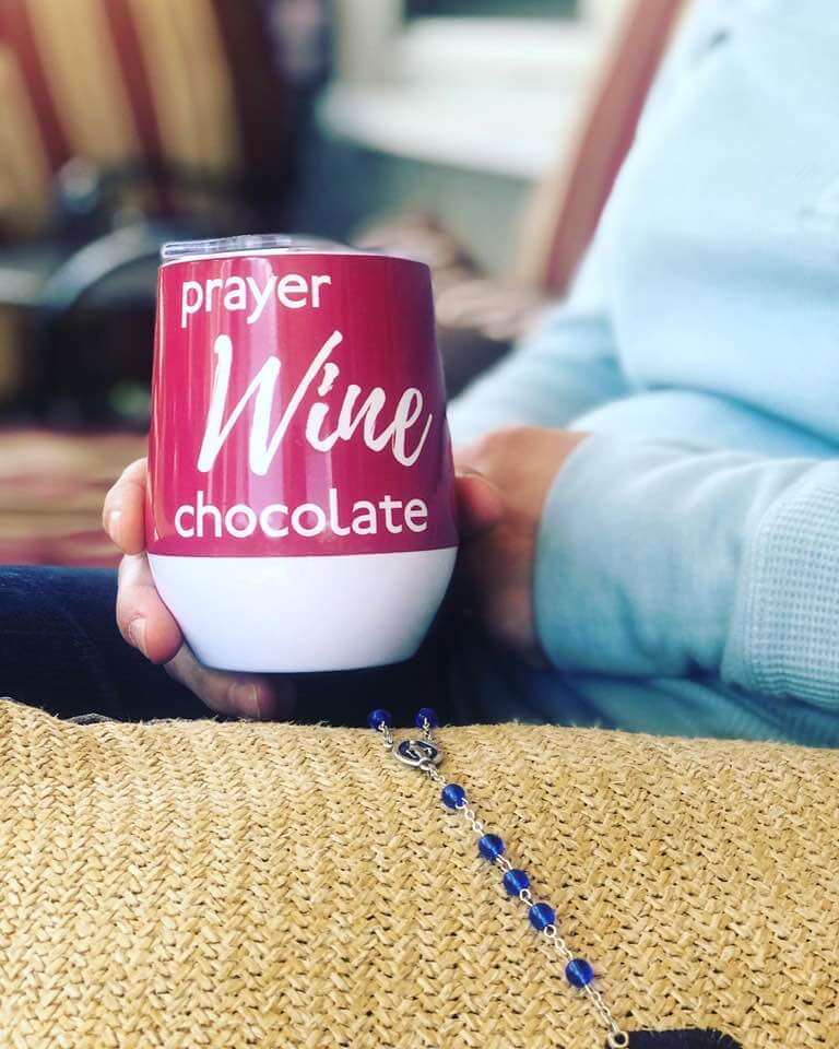 Close up of woman holding a Prayer Wine Chocolate tumbler and a rosary
