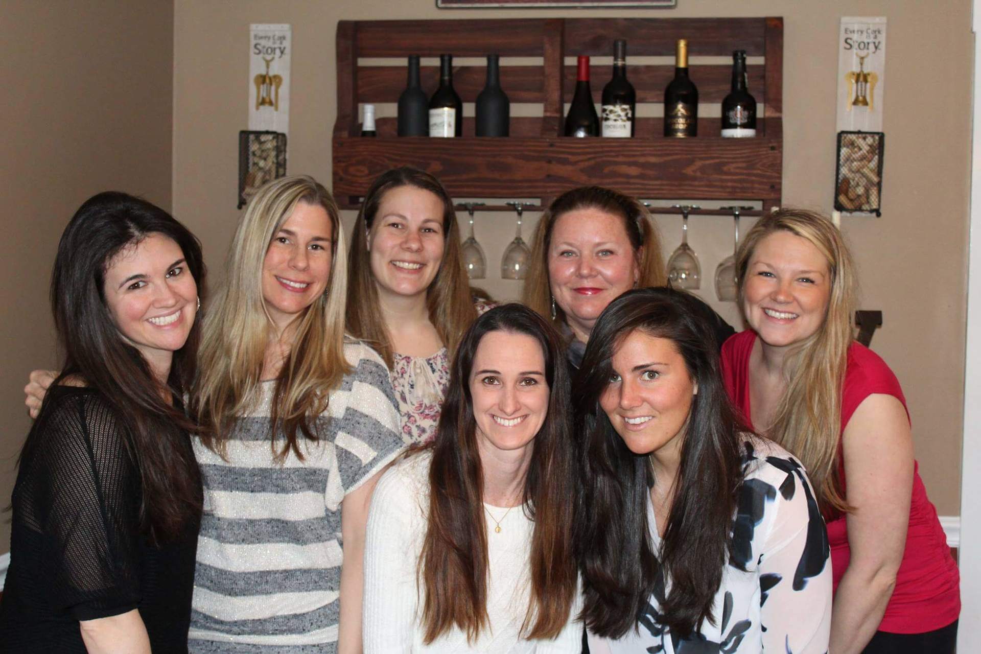7 women smiling in front of a wine rack
